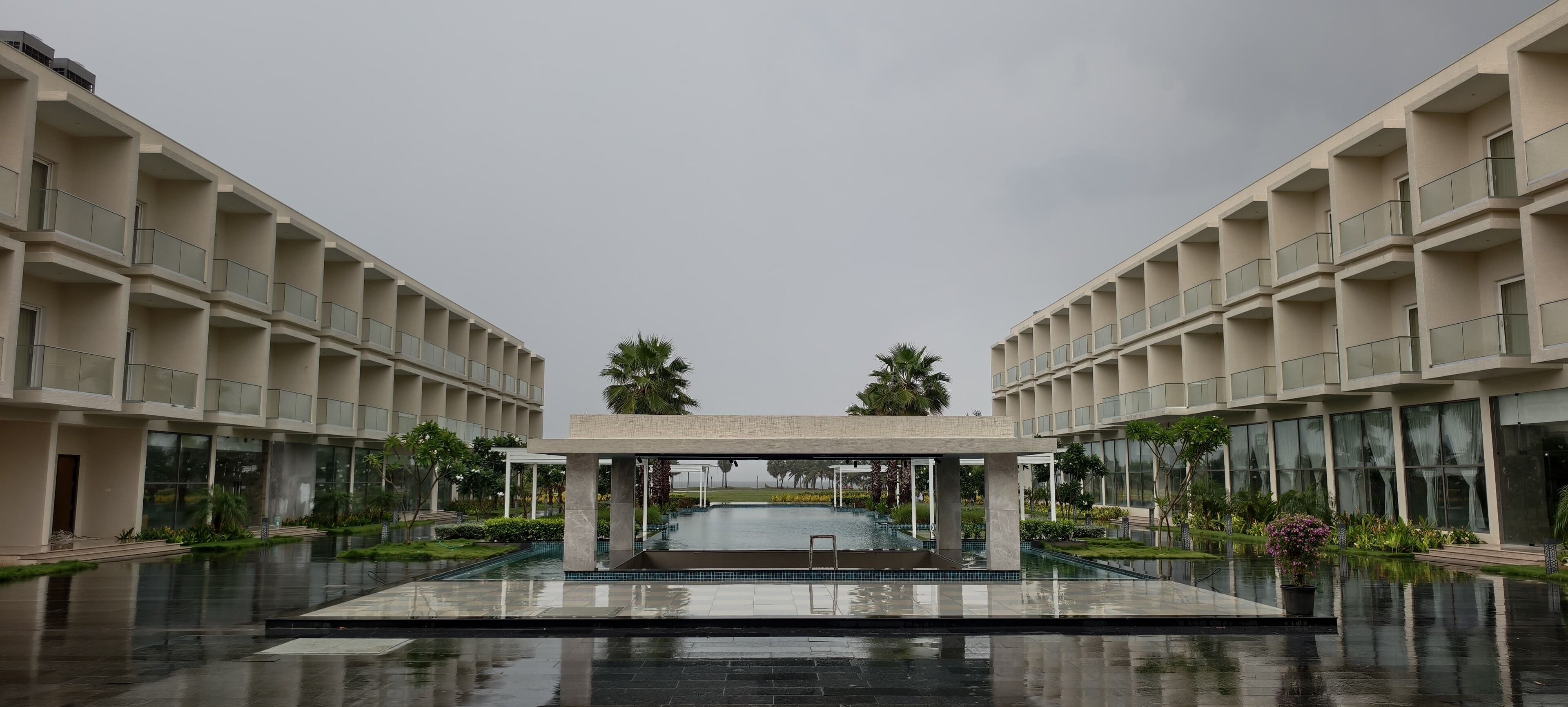 Un hotel moderno con piscina central, varios balcones y exuberante vegetación.