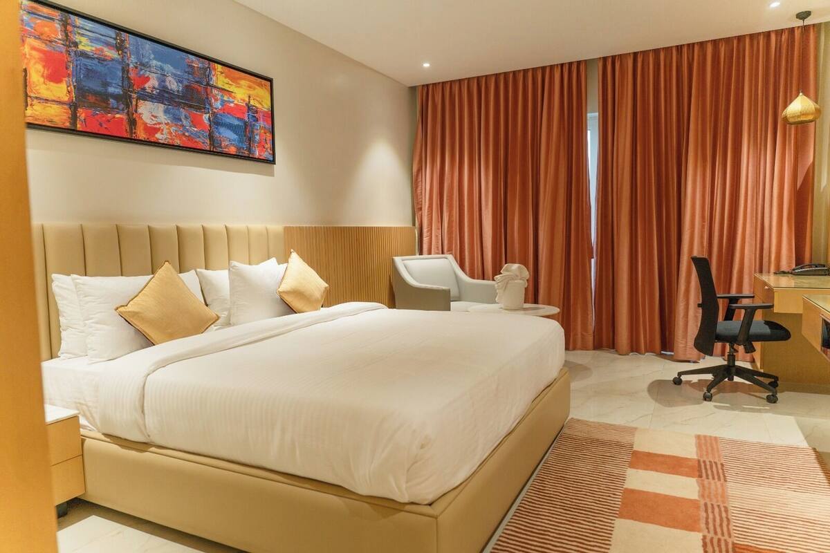 A hotel room with a large bed, a desk, a chair, and a painting on the wall.