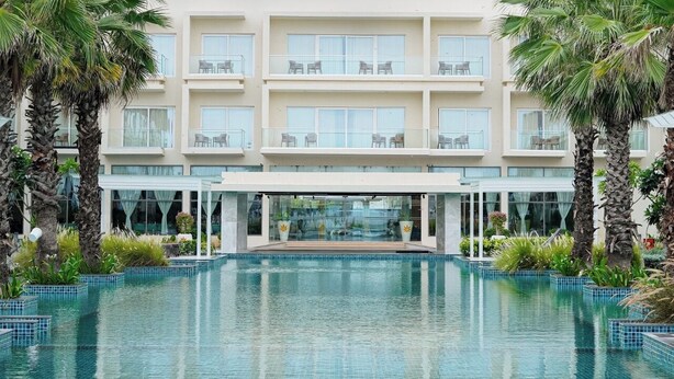 A hotel with a pool, multiple balconies, and palm trees. - Golden Sands - By The Bay Resorts (Bapatla)