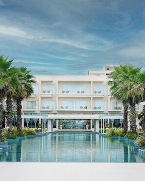 Un hotel con piscina, varios balcones y palmeras.