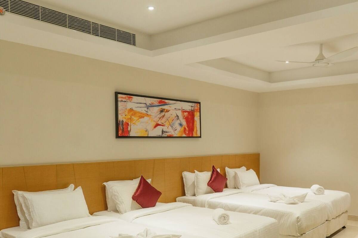 A hotel room with two beds, a ceiling fan, a painting on the wall, and a green and beige rug.