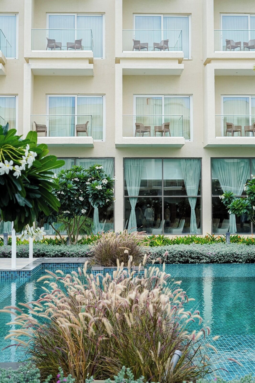 Un hotel con numerosi balconi, piscina e verdeggiante vegetazione.