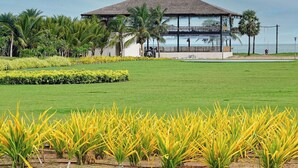 A modern building with a flat roof, surrounded by a well-maintained lawn and palm trees. - Golden Sands - By The Bay Resorts (Bapatla)