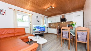 A compact living space with a sofa, dining table, chairs, a TV, kitchen area, and a window. - Ferienwohnung in Bensersiel (Esens)