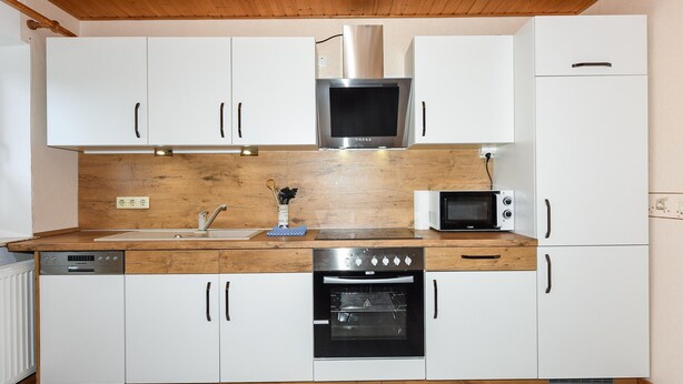 A compact kitchen with white cabinets, a wooden countertop, a stainless steel range hood, a microwave, a dishwasher, and an oven. - Ferienwohnung in Bensersiel (Esens)
