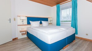 A bedroom with a bed, wooden headboard, bedside tables, and a window with curtains. - Ferienwohnung in Bensersiel (Esens)