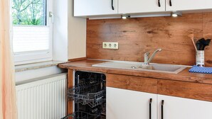 A kitchen with white cabinets, a wooden countertop, a built-in dishwasher, and a window with blinds. - Ferienwohnung in Bensersiel (Esens)
