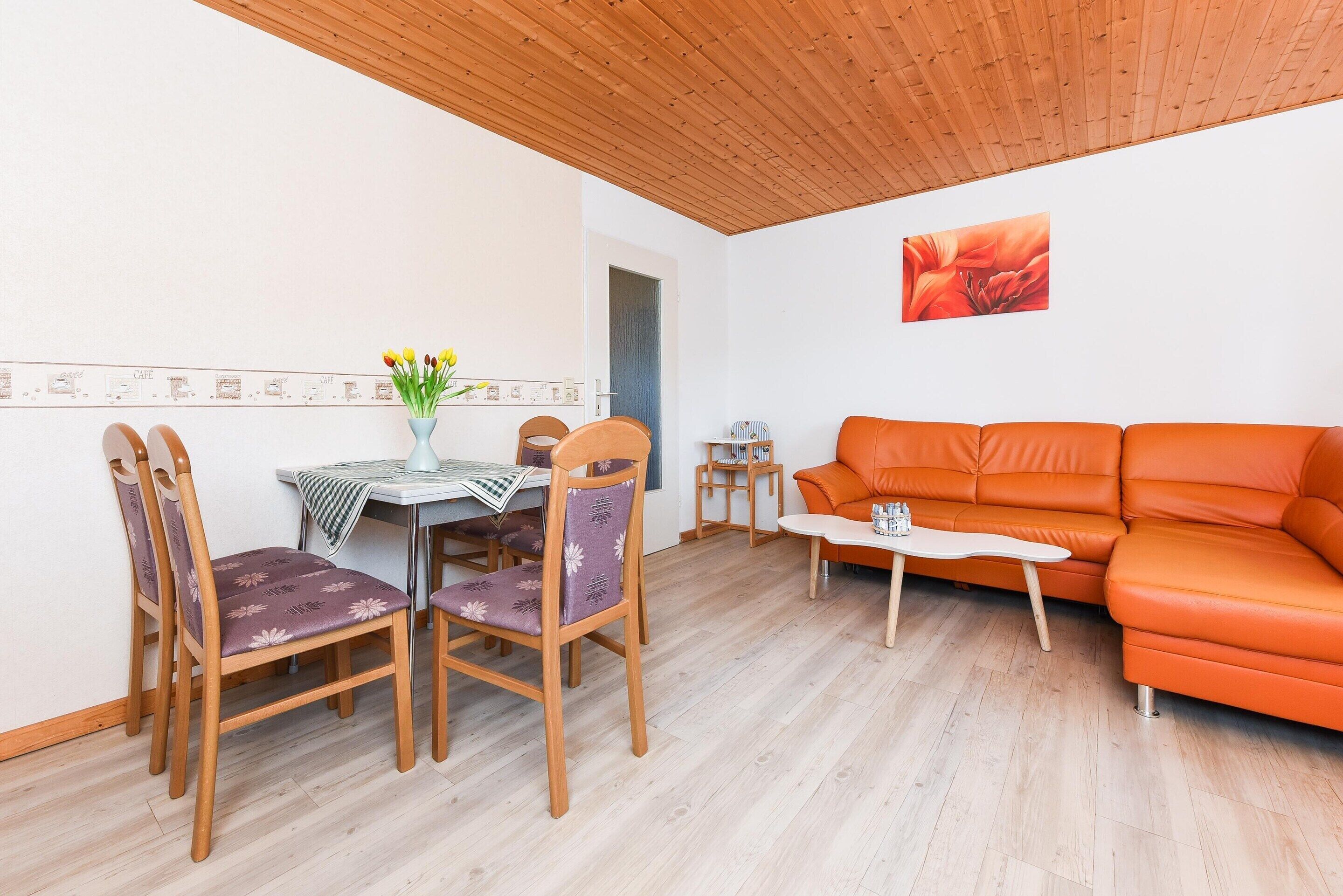 Een eetgedeelte met houten stoelen en een tafel, een oranje bank en een bijzettafeltje.