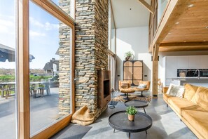 A spacious living area with a stone fireplace, comfortable seating, and a large window offering a view of the outdoors. - Luxurious and Sustainable 6-person Holiday Villa (De Koog)