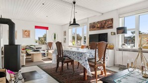 A dining area with a table set for four, surrounded by wicker chairs, a patterned rug, and a large window offering a view of the outside.
