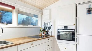 A kitchen with white cabinets, a wooden countertop, a stainless steel sink, a window, and a refrigerator. - 5 Star Holiday Home in Dronningmolle (Dronningmolle)