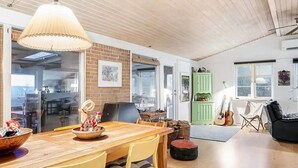 A spacious living area with a wooden dining table, yellow chairs, a green cabinet, and a guitar. - 5 Star Holiday Home in Dronningmolle (Dronningmolle)