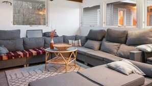 A cozy living room with a sectional sofa, a small round table, and a wicker chair. - 5 Star Holiday Home in Dronningmolle (Dronningmolle)