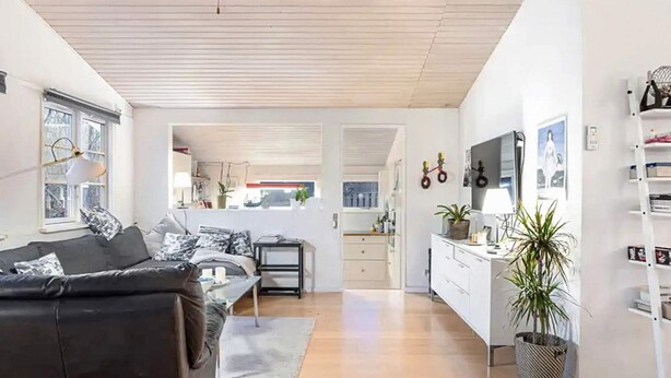 A modern living room with a black leather sofa, a dining area with a white table, and a kitchen with white cabinets. - 5 Star Holiday Home in Dronningmolle (Dronningmolle)