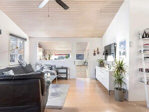 A modern living room with a black leather sofa, a dining area with a white table, and a kitchen with white cabinets. - 5 Star Holiday Home in Dronningmolle (Dronningmolle)