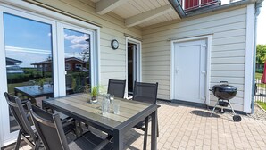 Een terras buiten met een tafel, stoelen, een barbecue en een schuifpui.