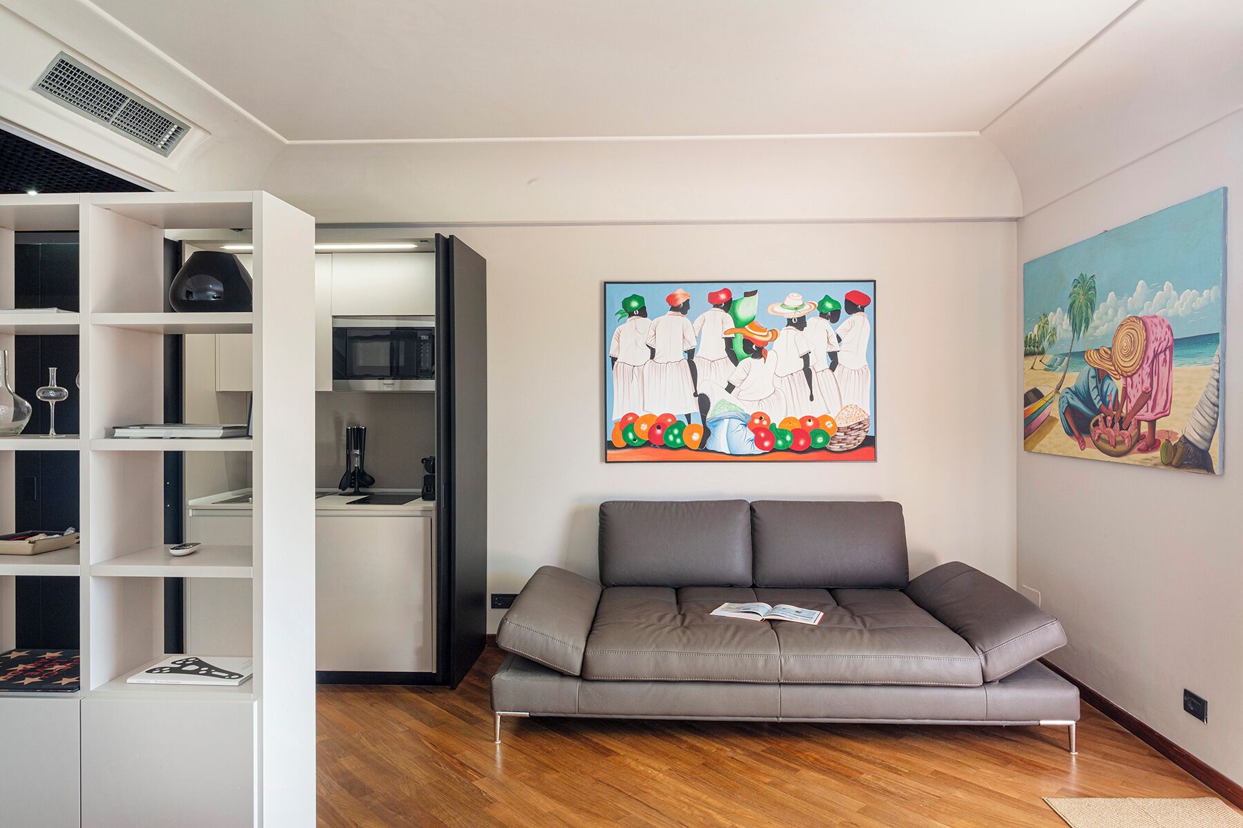 A modern living room with a grey sofa, white shelving, a microwave, and artwork on the walls.