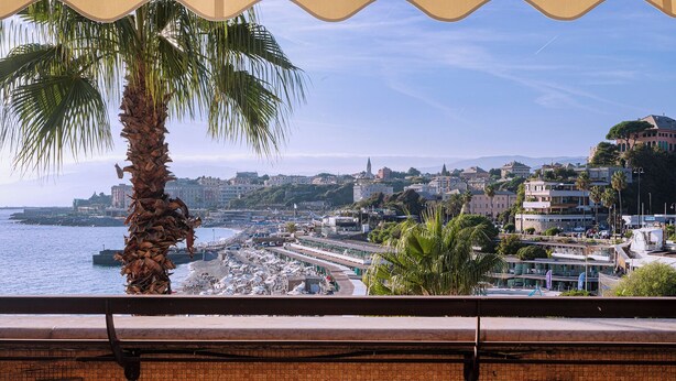 A coastal cityscape with a beach, buildings, and a palm tree. - Beachfront Studio with Terrace by Wonderful Italy (Genoa)