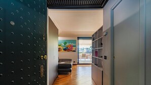 A hallway with a dark metal door, a grey sofa, wooden flooring, and a colorful painting on the wall. - Beachfront Studio with Terrace by Wonderful Italy (Genoa)