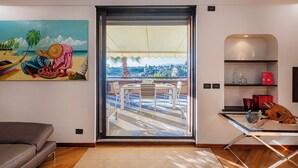 A modern living room with a large sliding glass door leading to a balcony with a city view. - Beachfront Studio with Terrace by Wonderful Italy (Genoa)