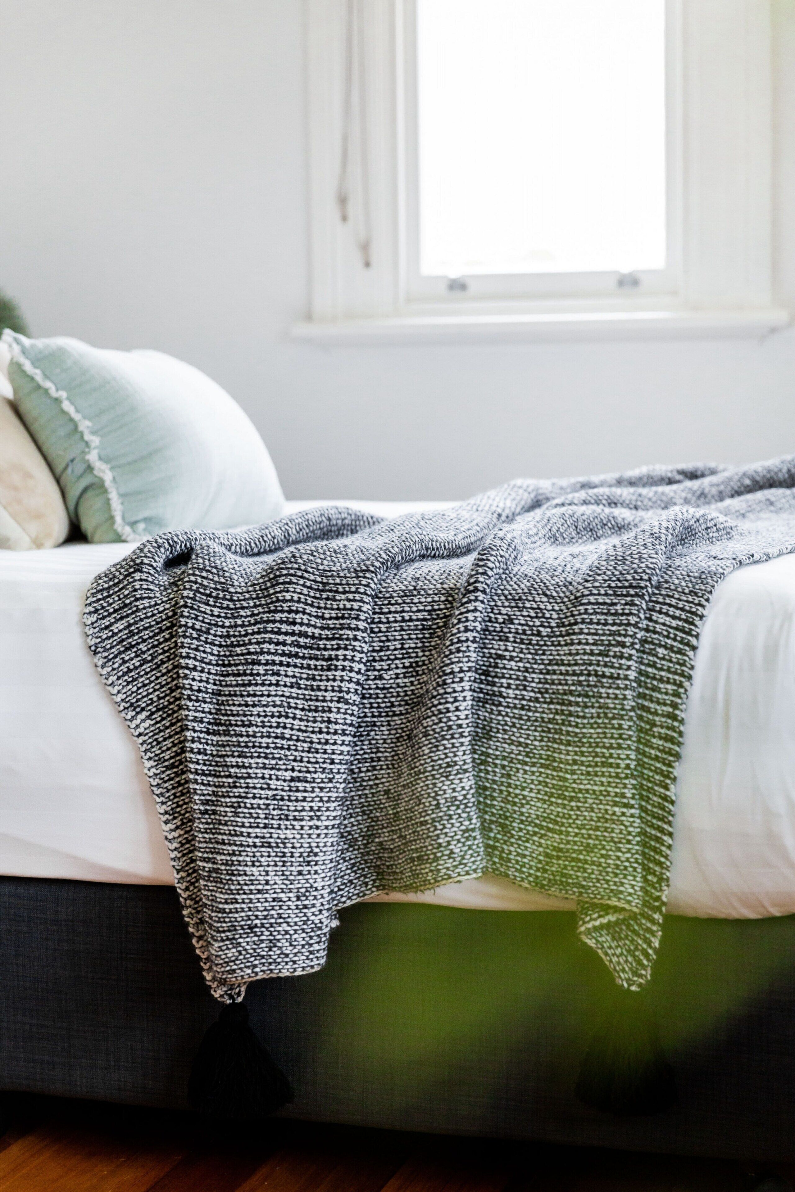 Un lit avec une couverture tricotée aux couleurs gris et blanc, un oreiller vert et un oreiller blanc.