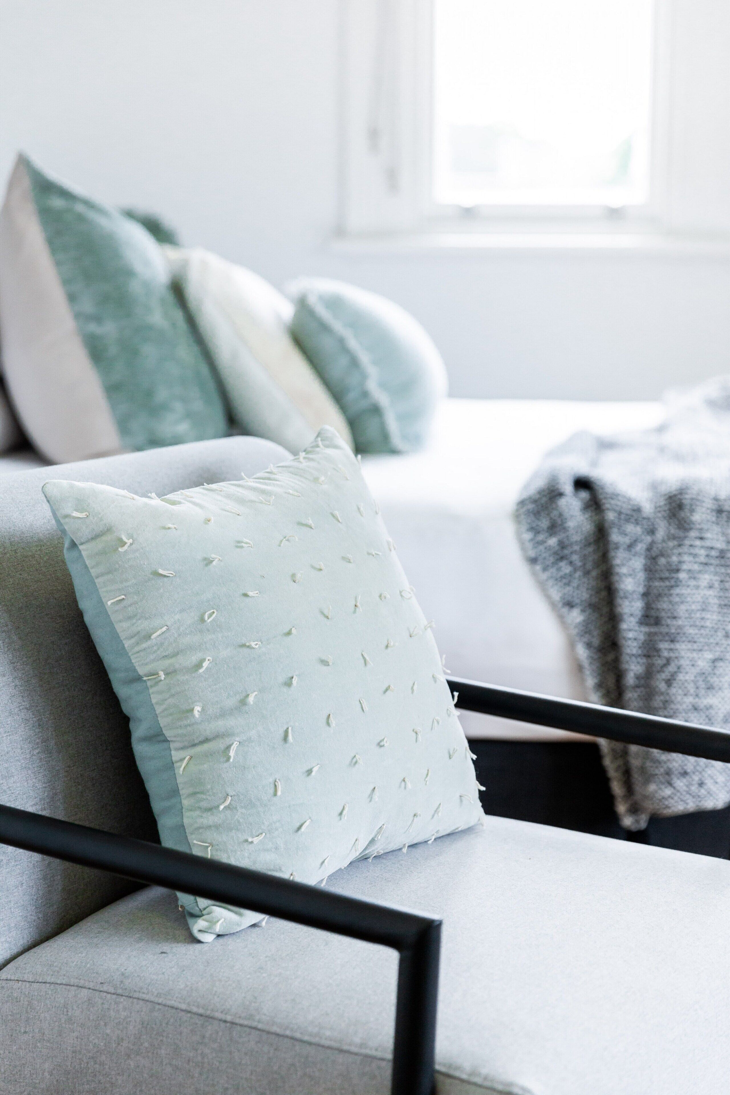 A modern living room with a grey sofa, a light blue pillow, and a grey throw blanket.