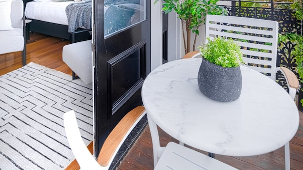 A balcony with a bed, a table with a plant, and a view of the city. - Designer Styled Studio in Central Trendy Glebe (Sydney)