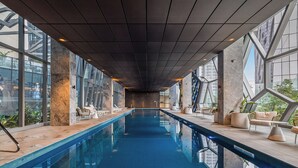 Une piscine intérieure moderne, de forme longue et étroite, dotée de grandes fenêtres et d’espaces aménagés le long des parois.