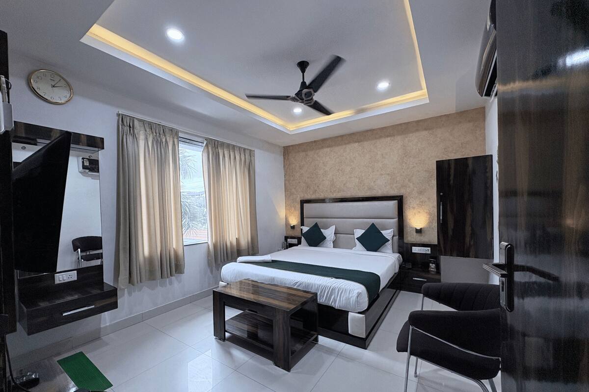 Une chambre d’hôtel moderne équipée d’un lit, de tables de chevet, d’un bureau, d’une chaise, d’un ventilateur de plafond et d’une fenêtre avec des rideaux.