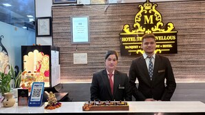 A hotel reception desk with a sign reading "Hotel The Marvelous" and "Banquet Hotel". There are framed certificates on the wall, a Paytm QR code, and a small statue of a deity. - Hotel the Marvellous (Jhansi)