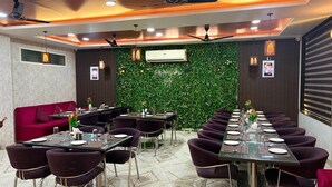 A restaurant with a long table, purple chairs, and a green wall with plants. - Hotel the Marvellous (Jhansi)