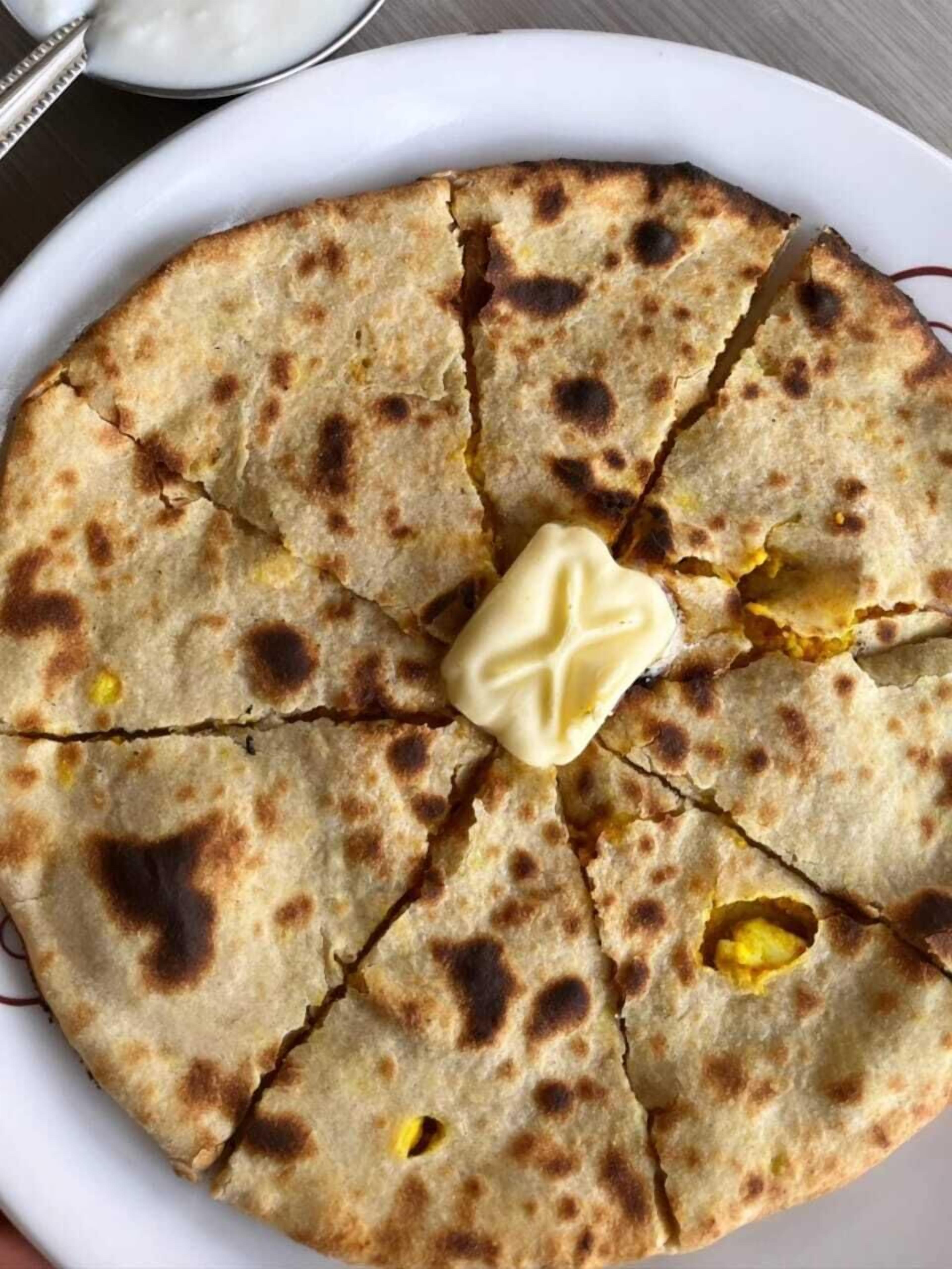Une galette ronde et plate, avec une noisette de beurre au centre, servie sur une assiette blanche.