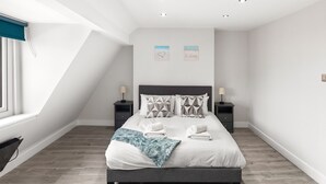 A modern bedroom with a bed, two nightstands, a window with blinds, and a ceiling light fixture. - Spacious 2-floor Flat Near Weymouth Seafront (Weymouth)