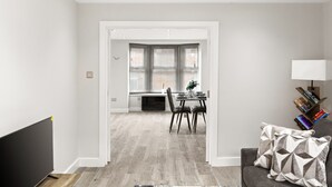 A modern living room with a flat-screen TV, a grey sofa, and a dining area with a table and chairs. - Spacious 2-floor Flat Near Weymouth Seafront (Weymouth)