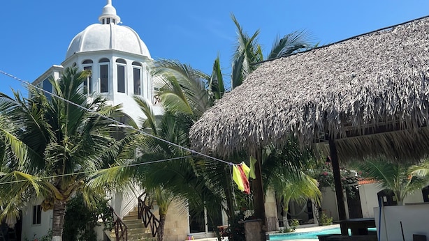 A white building with a dome and a thatched structure.