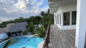 A swimming pool with a wooden deck and a thatched-roof structure in the background.