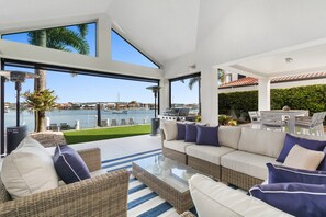 A modern outdoor living area with a white sofa, wicker furniture, and a glass coffee table. - Amazing Canal House With Private Jetty, Gym & Pool (Sunshine Coast)