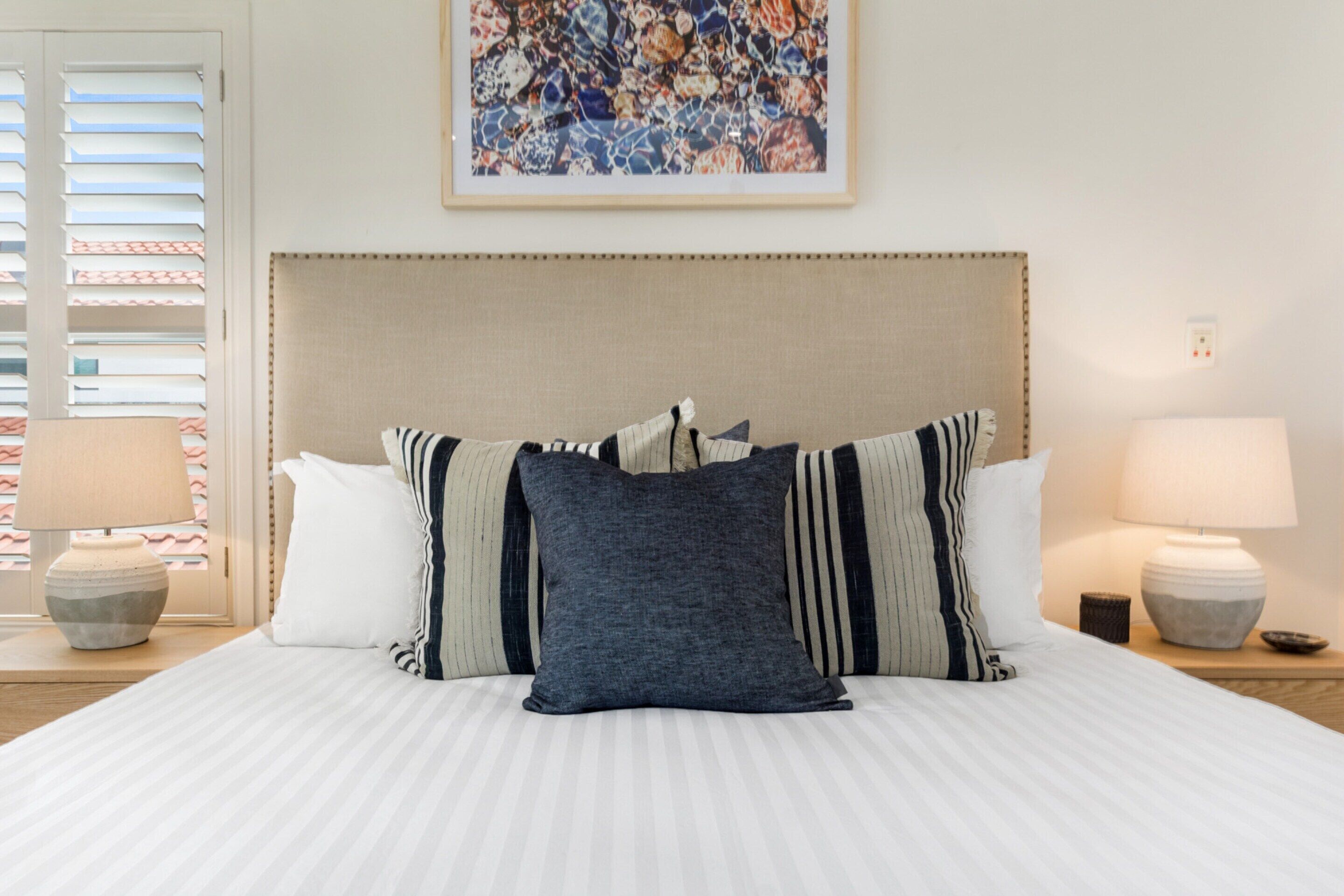 A neatly made bed with striped pillows, a headboard, and a framed artwork above.