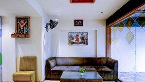 A living room with a sofa, a chair, a coffee table, a wall-mounted fan, and a clock.