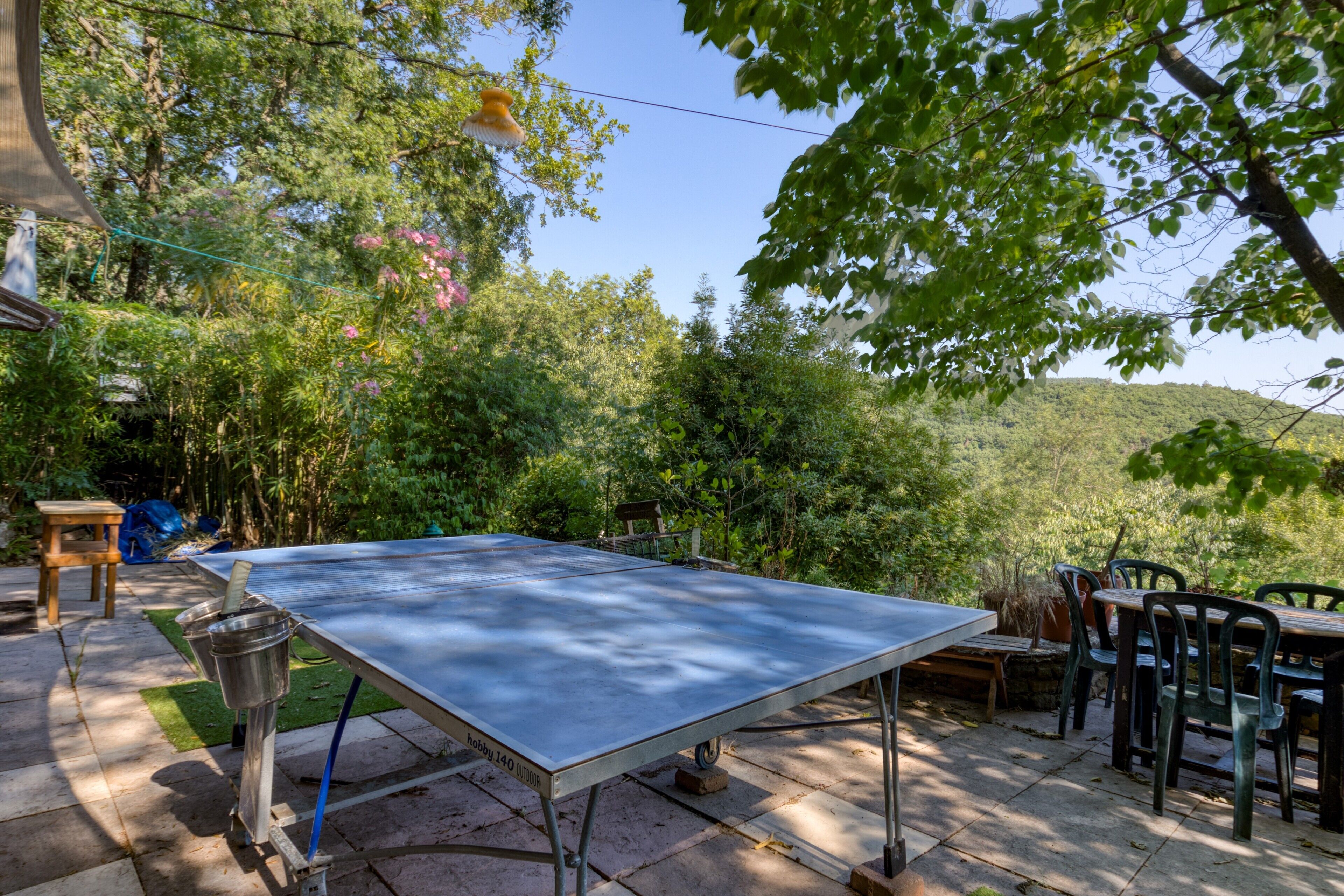 Una mesa de ping pong al aire libre en un jardín, con una mesa y sillas cerca.