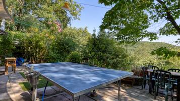 Una mesa de ping pong al aire libre en un jardín, con una mesa y sillas cerca.