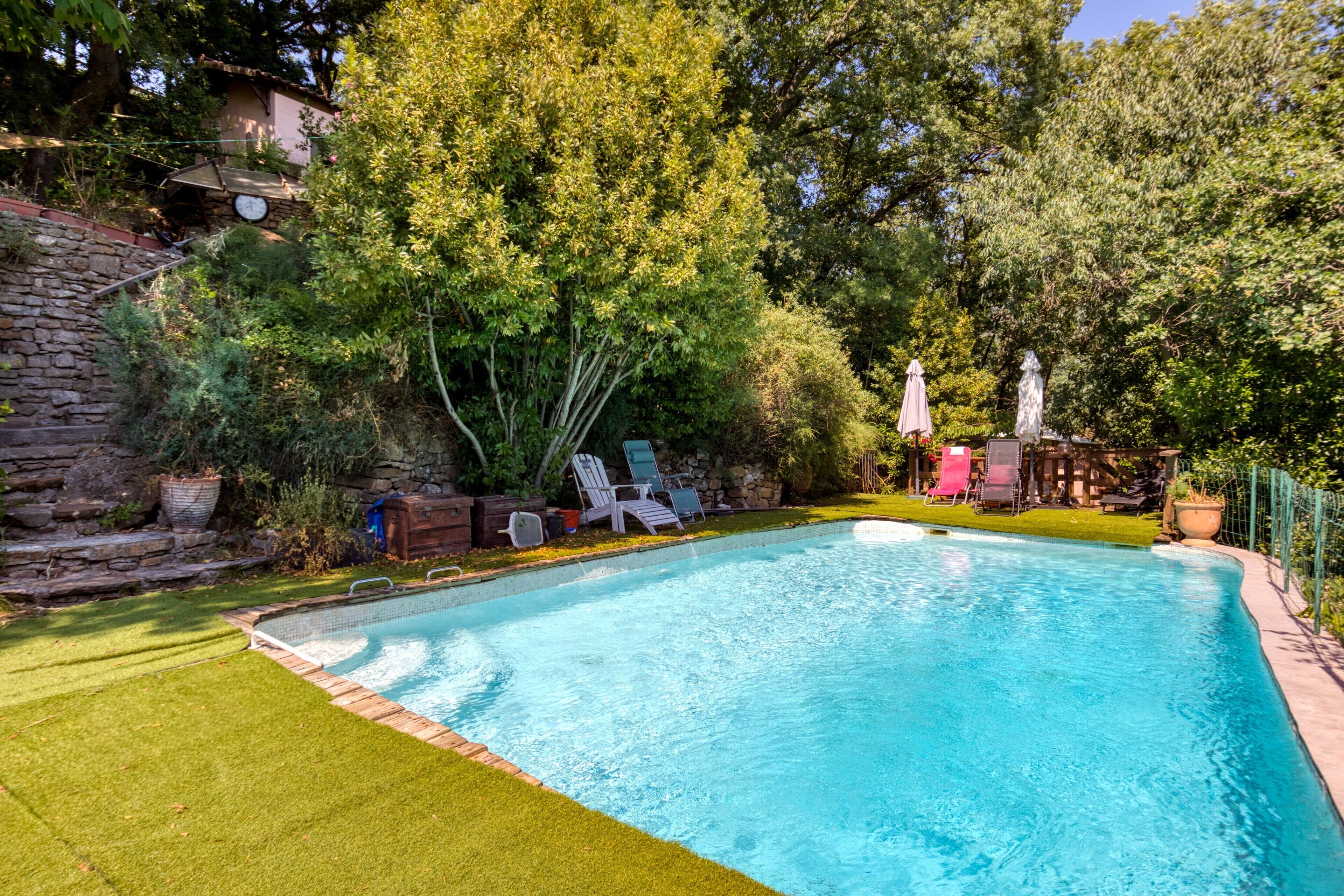 A rectangular swimming pool with a stone wall on one side and a grassy area on the other.
