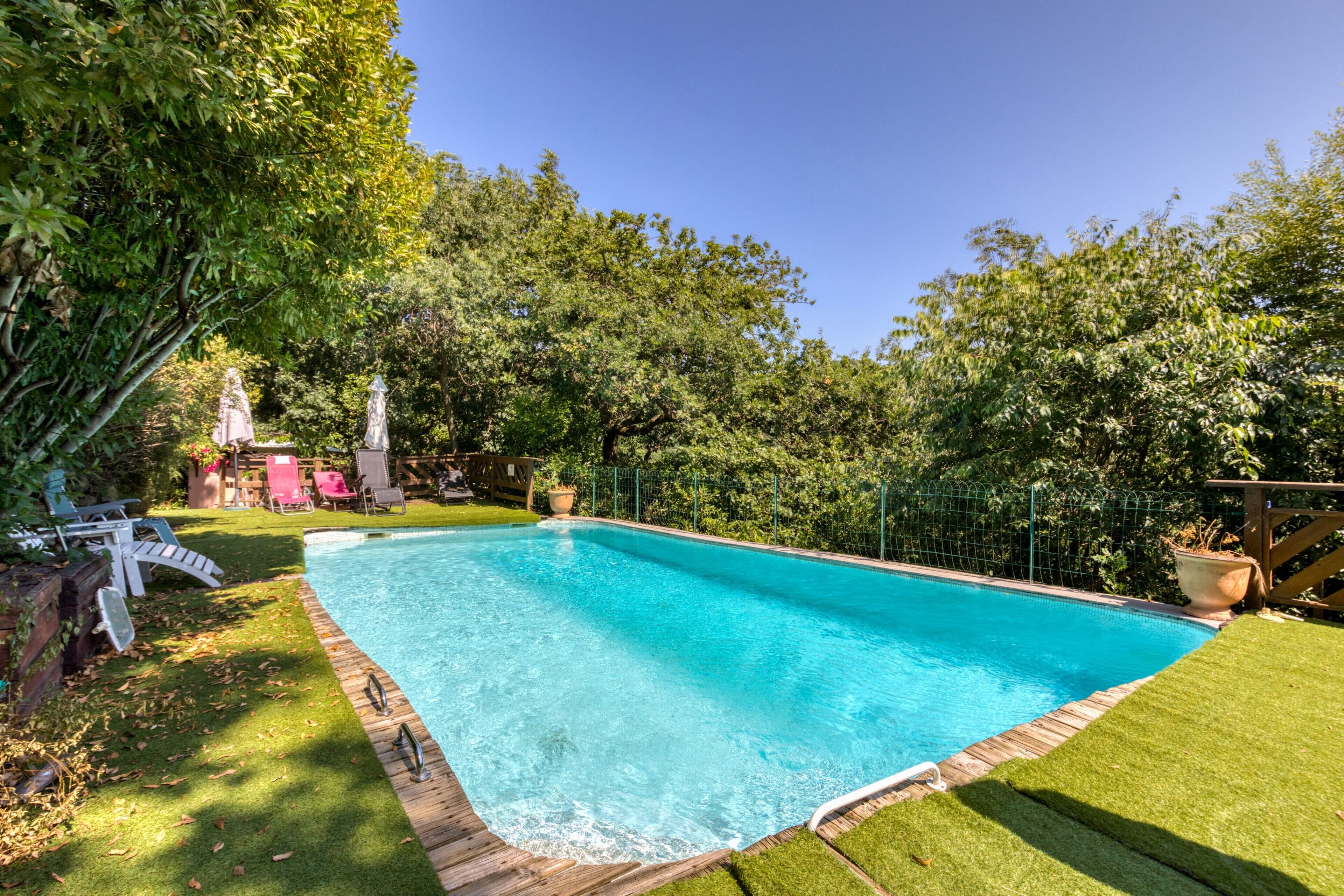 Une piscine rectangulaire bordée d’une terrasse en bois, entourée d’une pelouse verdoyante et d’arbres.