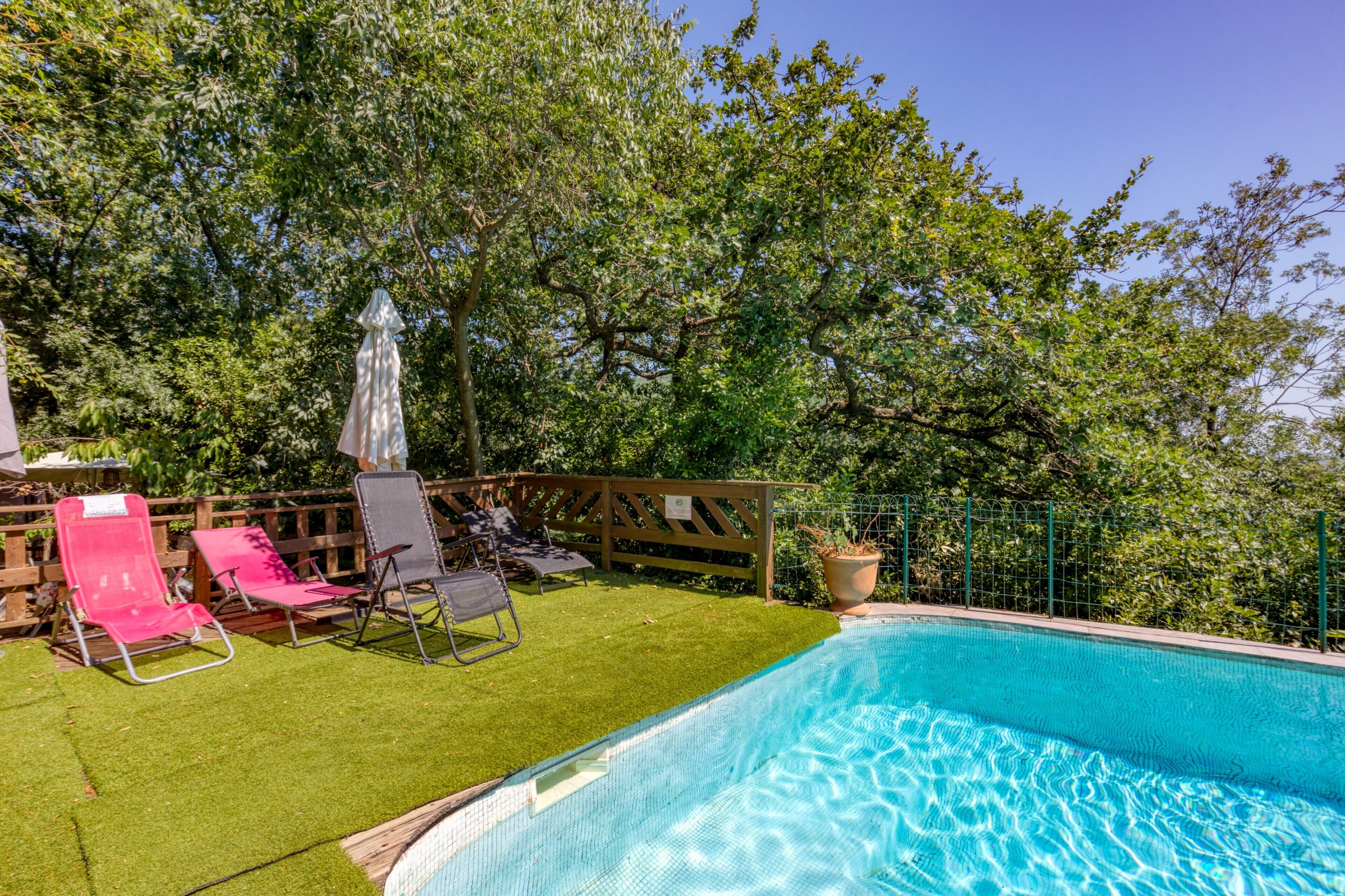 A swimming pool with a wooden deck, surrounded by trees and a fence.