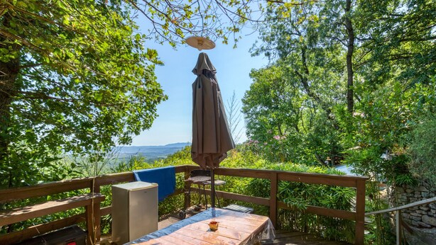 A wooden deck with a table and chairs, an umbrella, and a view of a natural landscape. - Gite du haut – in La Rouquette, a charming little hamlet (Saint-Privat)