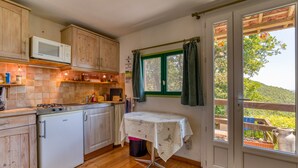 A compact kitchen with wooden cabinets, a microwave, a stove, and a table with a tablecloth. - Gite du haut – in La Rouquette, a charming little hamlet (Saint-Privat)