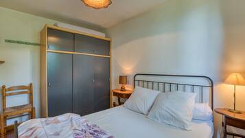 A bedroom with a bed, a wardrobe, a chair, and a bedside table with a lamp.