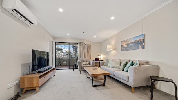 A modern living room with a flat-screen TV, a wooden coffee table, a sofa, and a small table. - Central 2-bed Apartment With Pool, Gym and Spa (Canberra)