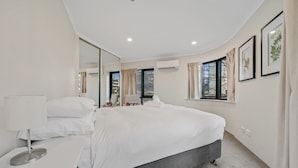 A modern bedroom with a large bed, a bedside table, a mirror, and a window with curtains. - Central 2-bed Apartment With Pool, Gym and Spa (Canberra)
