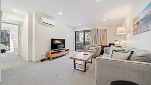 A modern living room with a flat-screen TV, a wooden coffee table, a grey sofa, and a large window with curtains. - Central 2-bed Apartment With Pool, Gym and Spa (Canberra)